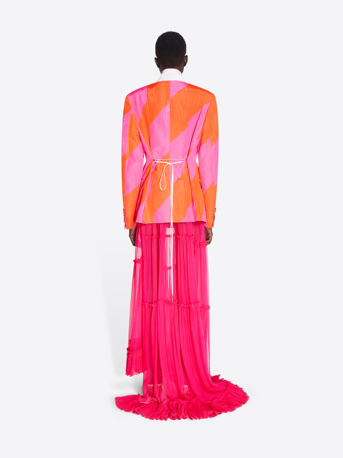 Person wearing a vibrant, geometric-patterned outfit with an orange and pink jacket and pink skirt on a white background. - Dries Van Noten