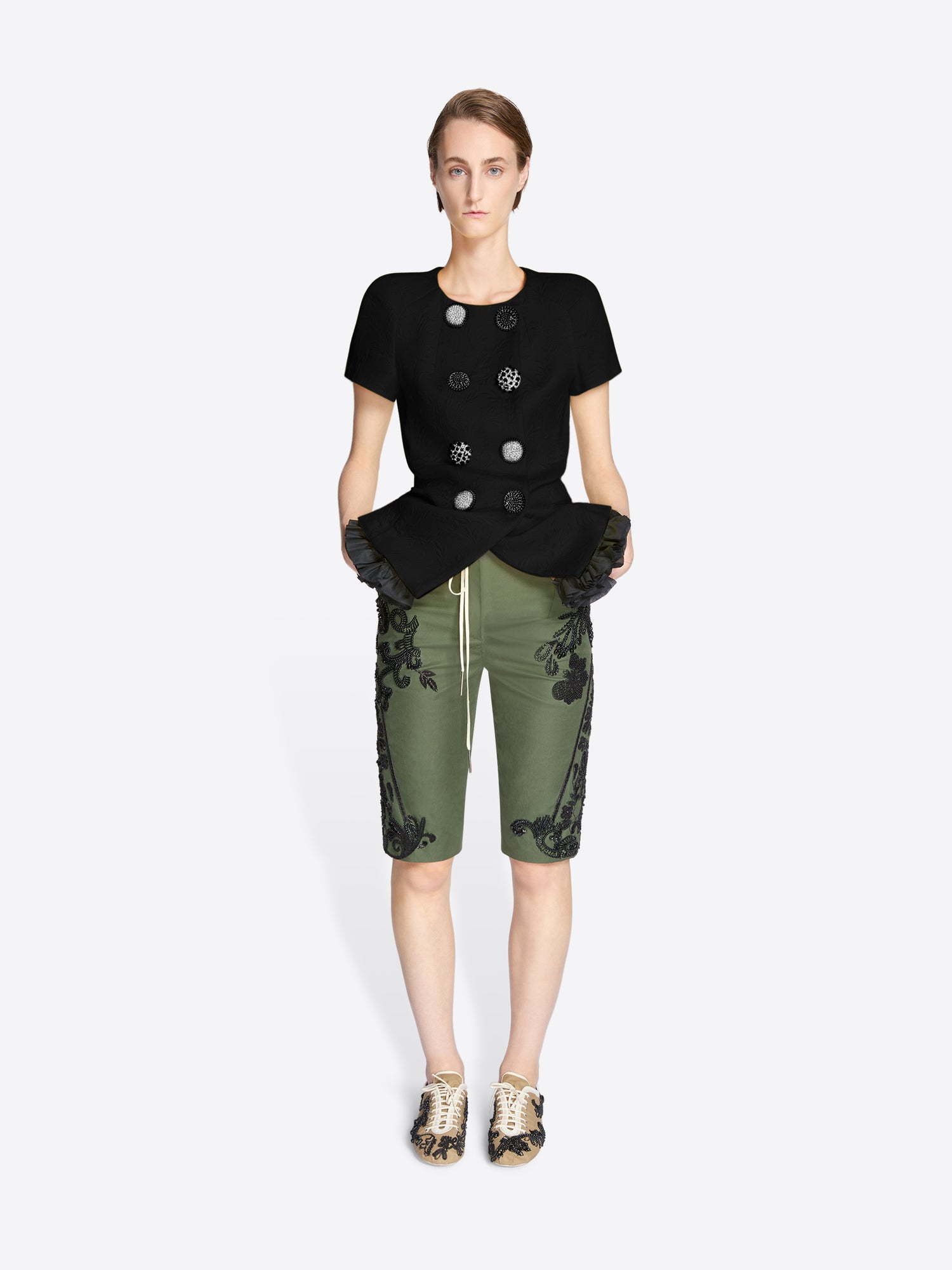 Woman wearing a black top with decorative buttons and green pants with floral patterns on a white background - Dries Van Noten