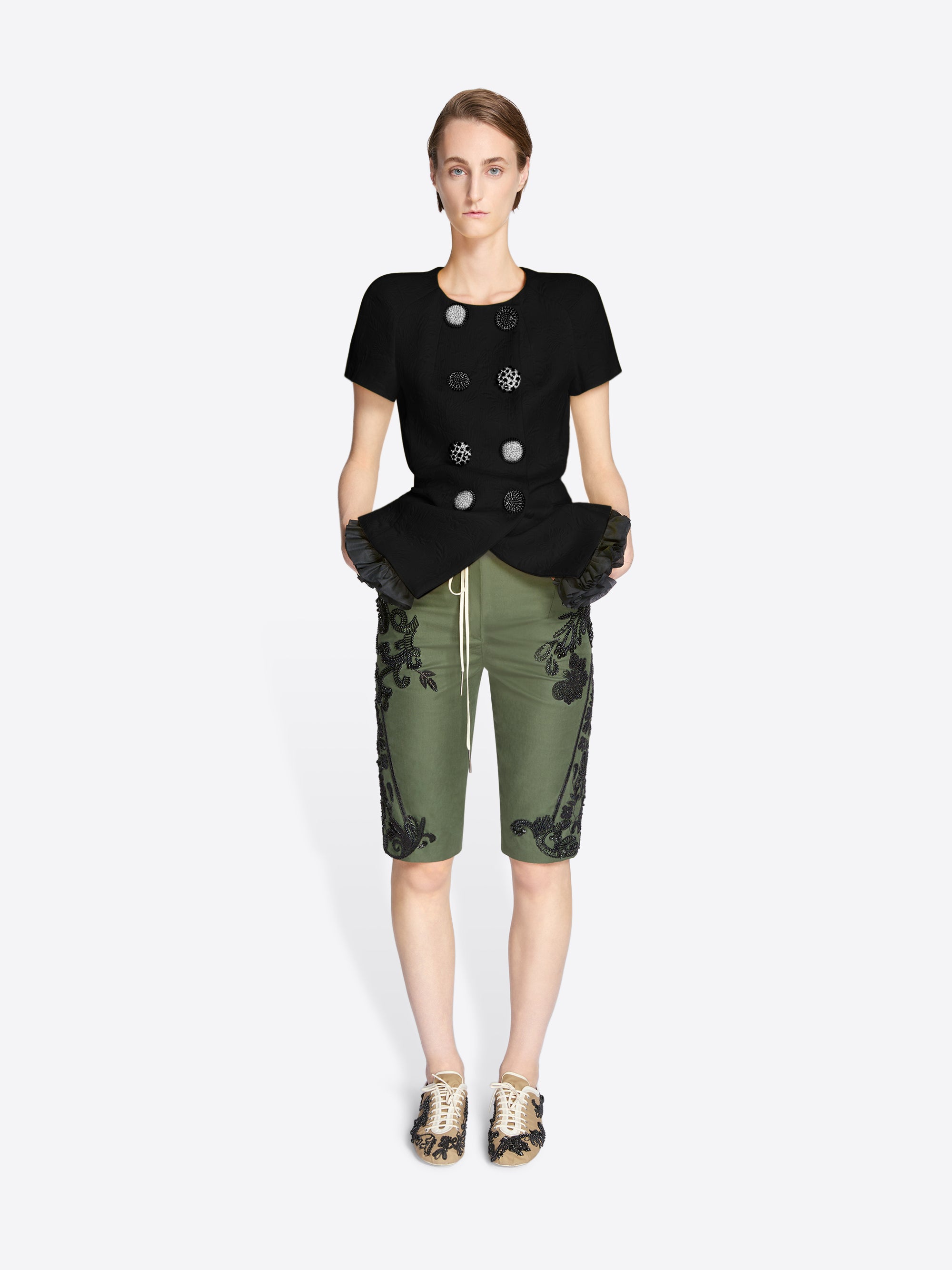 Woman wearing a black top with decorative buttons and green pants with floral patterns on a white background - Dries Van Noten