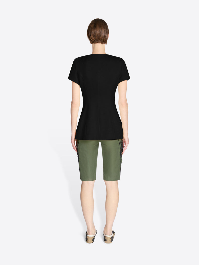 Person wearing a black t-shirt and green shorts on a white background - Dries Van Noten