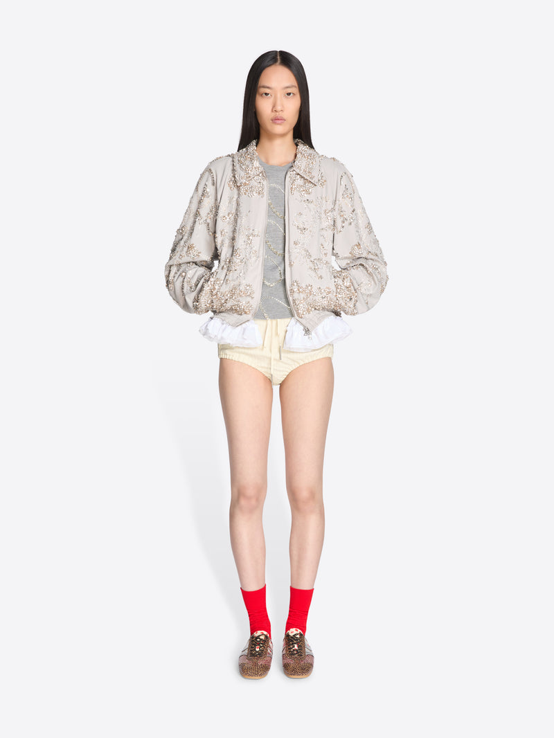 Person wearing a patterned jacket, gray shirt, yellow shorts, and red socks on a white background - Dries Van Noten