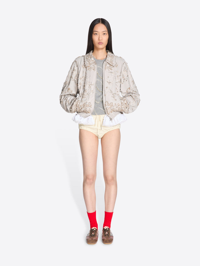 Person wearing a patterned jacket, gray shirt, yellow shorts, and red socks on a white background - Dries Van Noten