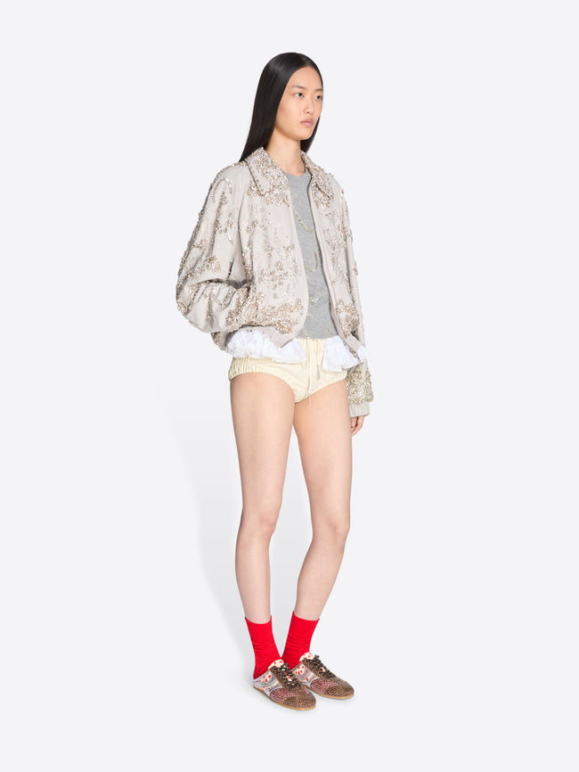 Person wearing a patterned jacket, light-colored shorts, and red socks on a white background - Dries Van Noten