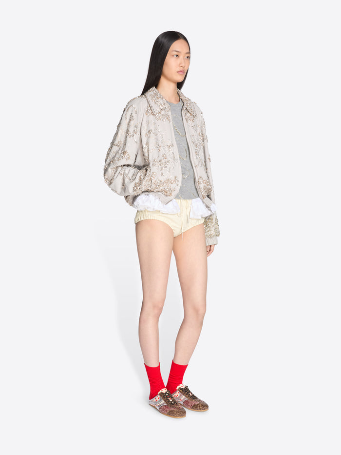 Person wearing a patterned jacket, light-colored shorts, and red socks on a white background - Dries Van Noten
