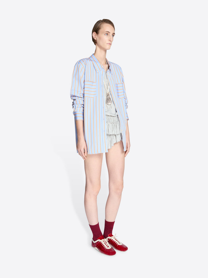 Person wearing a light blue striped shirt, shorts, and red sneakers on a white background - Dries Van Noten