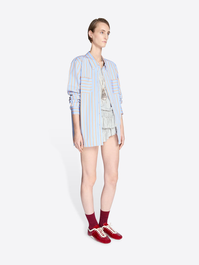 Person wearing a light blue striped shirt, shorts, and red sneakers on a white background - Dries Van Noten