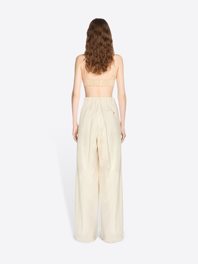 Woman wearing a strapless top and beige wide-leg pants on a white background - Dries Van Noten