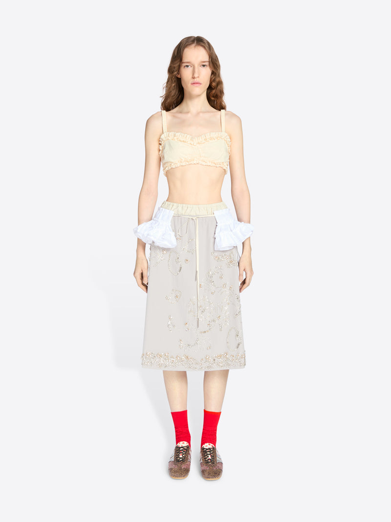 Woman wearing a light-colored top and skirt with red socks on a white background - Dries Van Noten