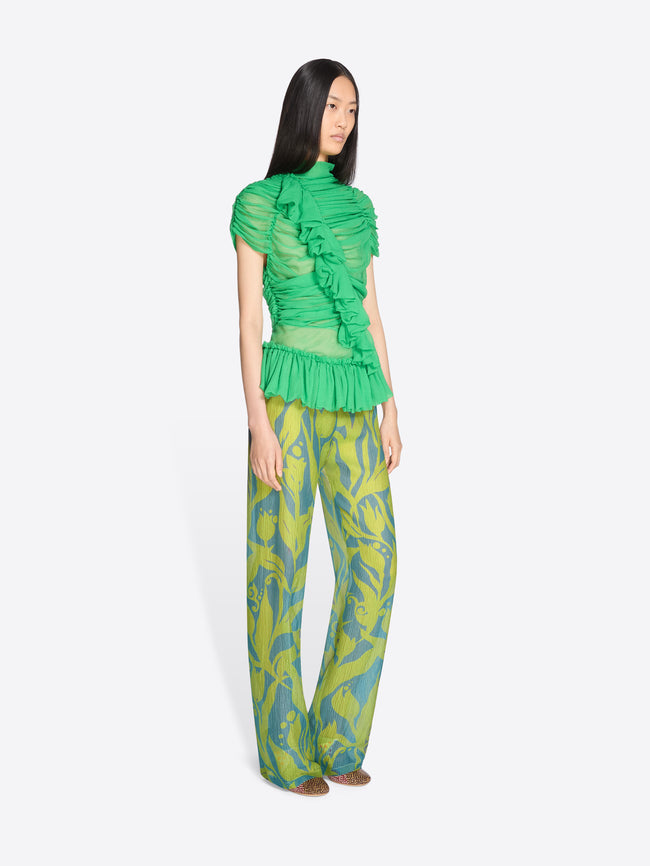 Model wearing a green ruffled top and patterned pants on a white background - Dries Van Noten