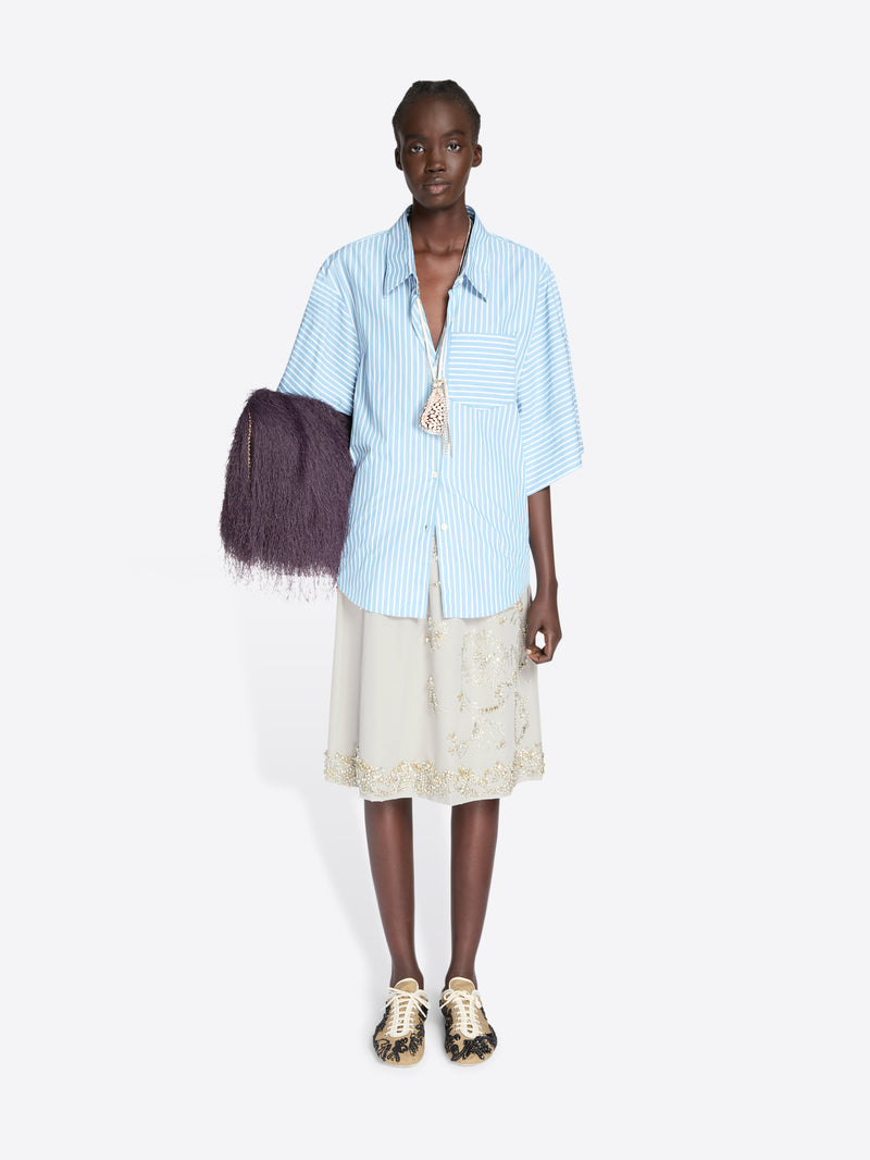 Model wearing a light blue striped shirt and beige skirt with a dark purple bag on a white background - Dries Van Noten