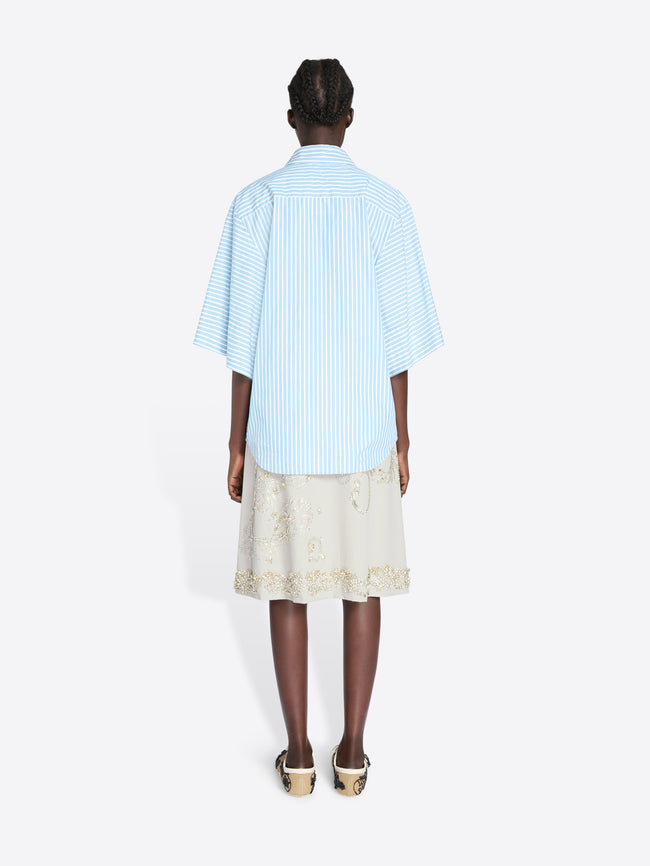 Person wearing a light blue striped shirt and beige skirt on a white background - Dries Van Noten