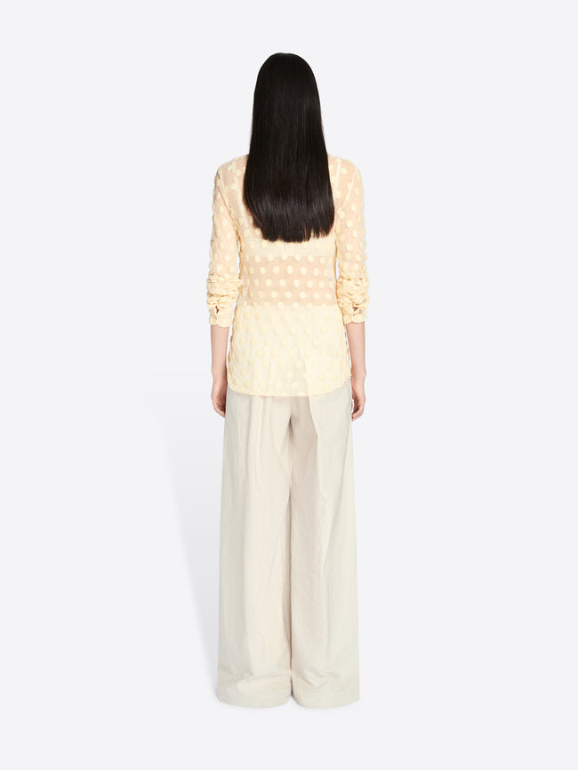 Person wearing a light yellow top and beige pants on a white background - Dries Van Noten
