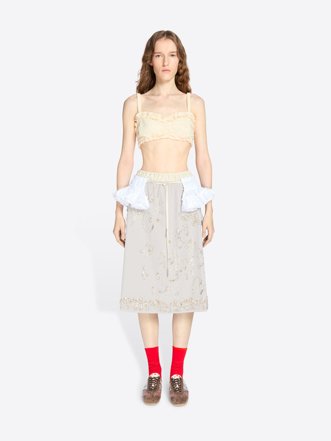 Woman wearing a light-colored top and skirt with red socks on a white background - Dries Van Noten