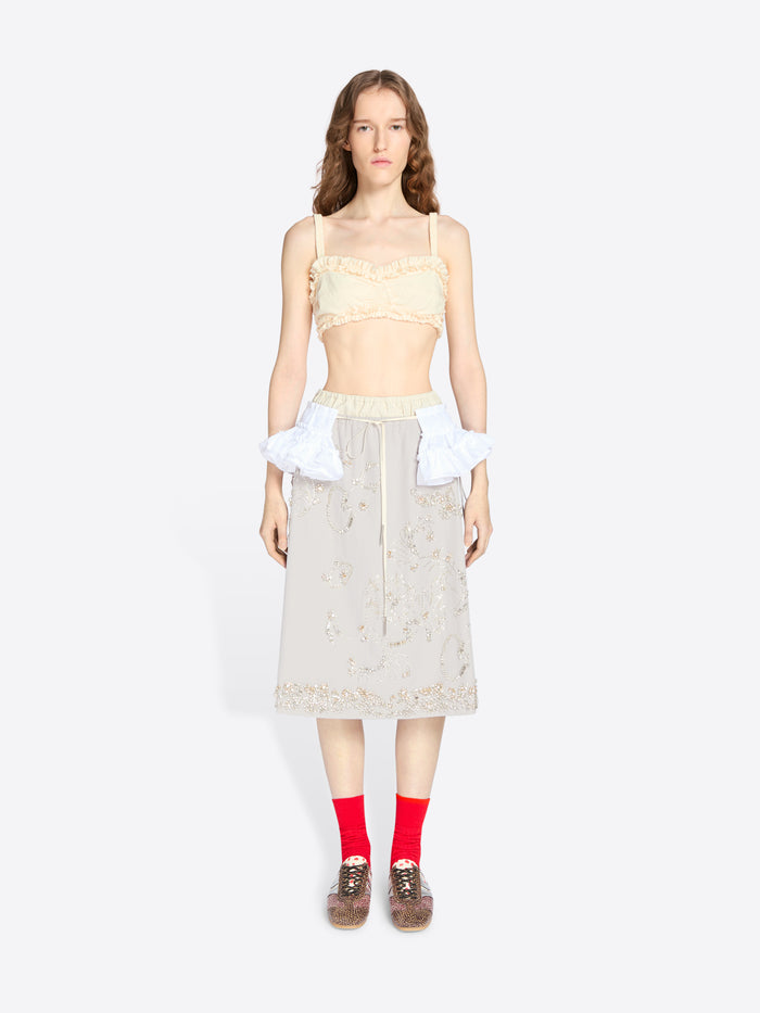 Woman wearing a light-colored top and skirt with red socks on a white background - Dries Van Noten