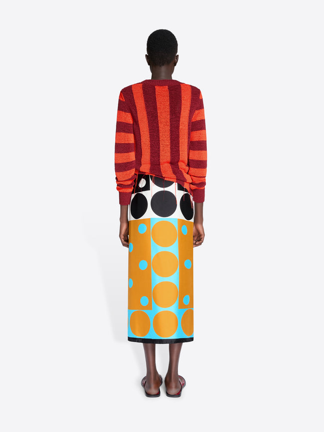 Person wearing a red and orange striped sweater and a colorful skirt with large polka dots on a white background - Dries Van Noten
