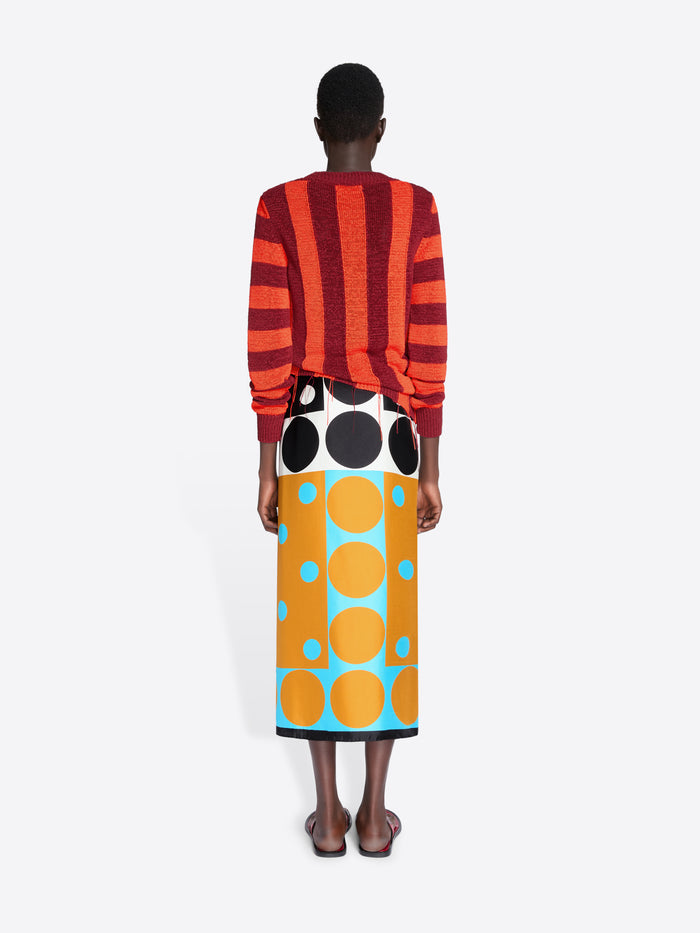 Person wearing a red and orange striped sweater and a colorful skirt with large polka dots on a white background - Dries Van Noten