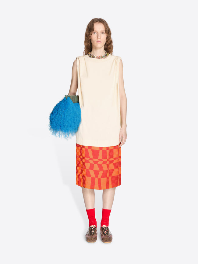 Woman wearing a beige sleeveless top and red patterned skirt, holding a blue feathered bag on a white background. - Dries Van Noten
