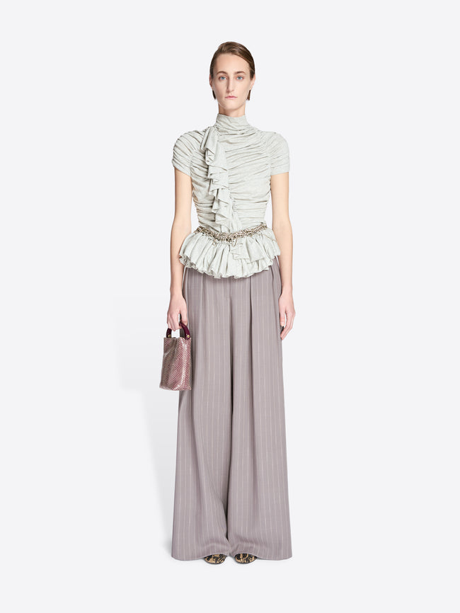 Woman wearing a light green ruffled top and gray wide-leg pants on a white background - Dries Van Noten