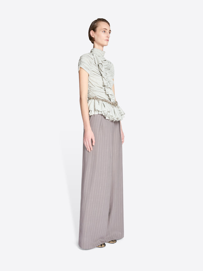 Woman wearing a light green ruffled top and gray pleated skirt on a white background - Dries Van Noten