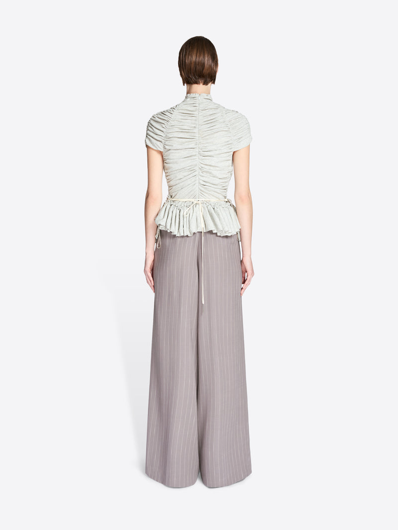 Person wearing a light green ruched top and gray wide-leg pants on a white background - Dries Van Noten