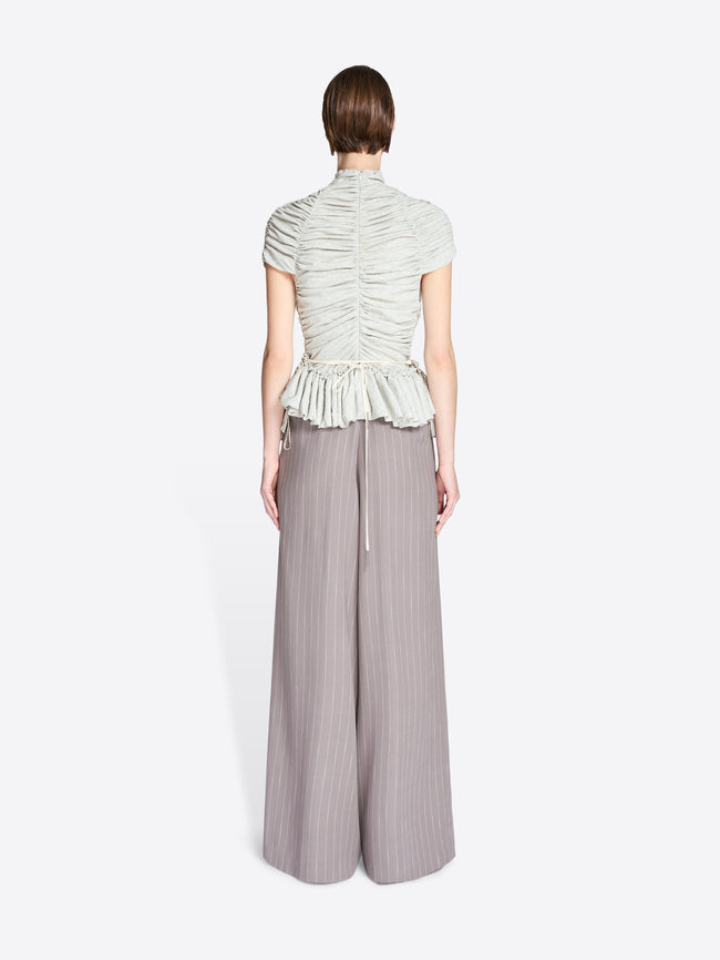 Person wearing a light green ruched top and gray wide-leg pants on a white background - Dries Van Noten