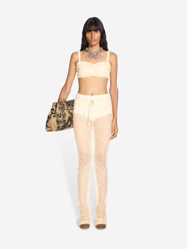 Woman wearing a light yellow outfit with polka dot pants and a matching top, holding a patterned handbag on a white background. - Dries Van Noten