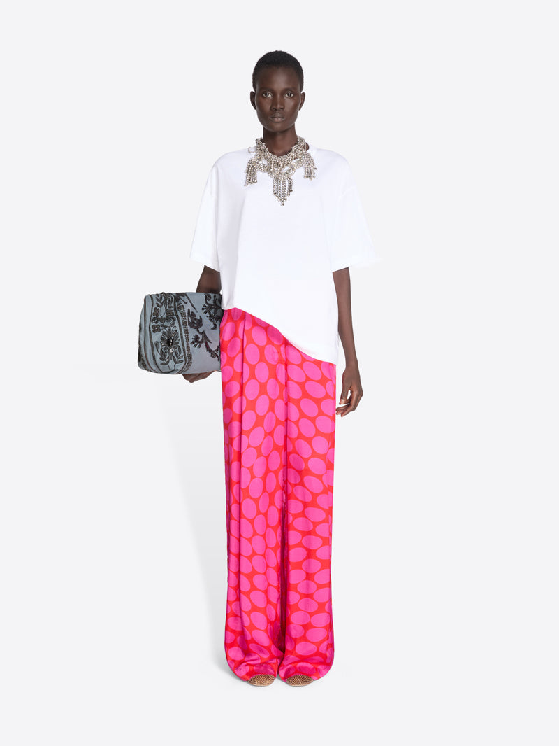 Model wearing a white top and pink pants with a pattern, holding a gray clutch on a white background - Dries Van Noten