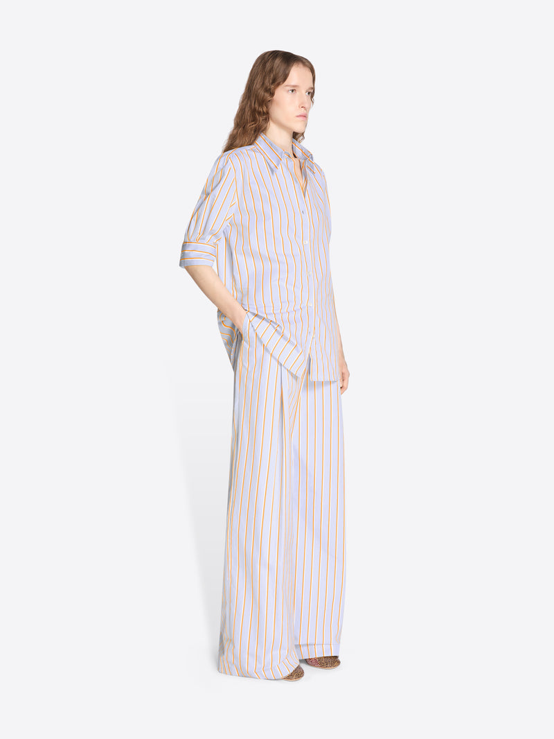 Person wearing a long, light-colored striped shirt and pants on a white background - Dries Van Noten