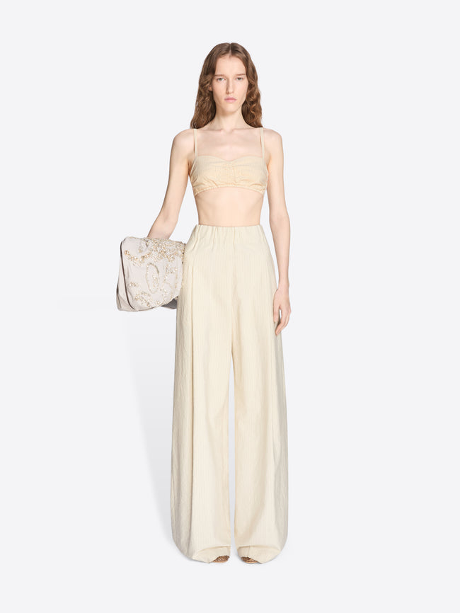 Woman wearing a light-colored strapless top and wide-leg pants, holding a matching handbag on a white background. - Dries Van Noten
