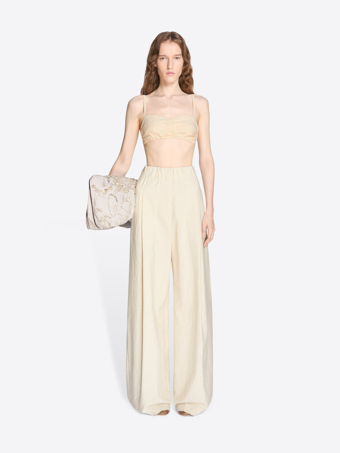 Woman wearing a light-colored strapless top and wide-leg pants, holding a matching handbag on a white background. - Dries Van Noten