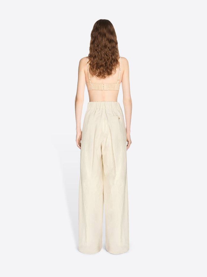Woman wearing a strapless top and beige wide-leg pants on a white background - Dries Van Noten