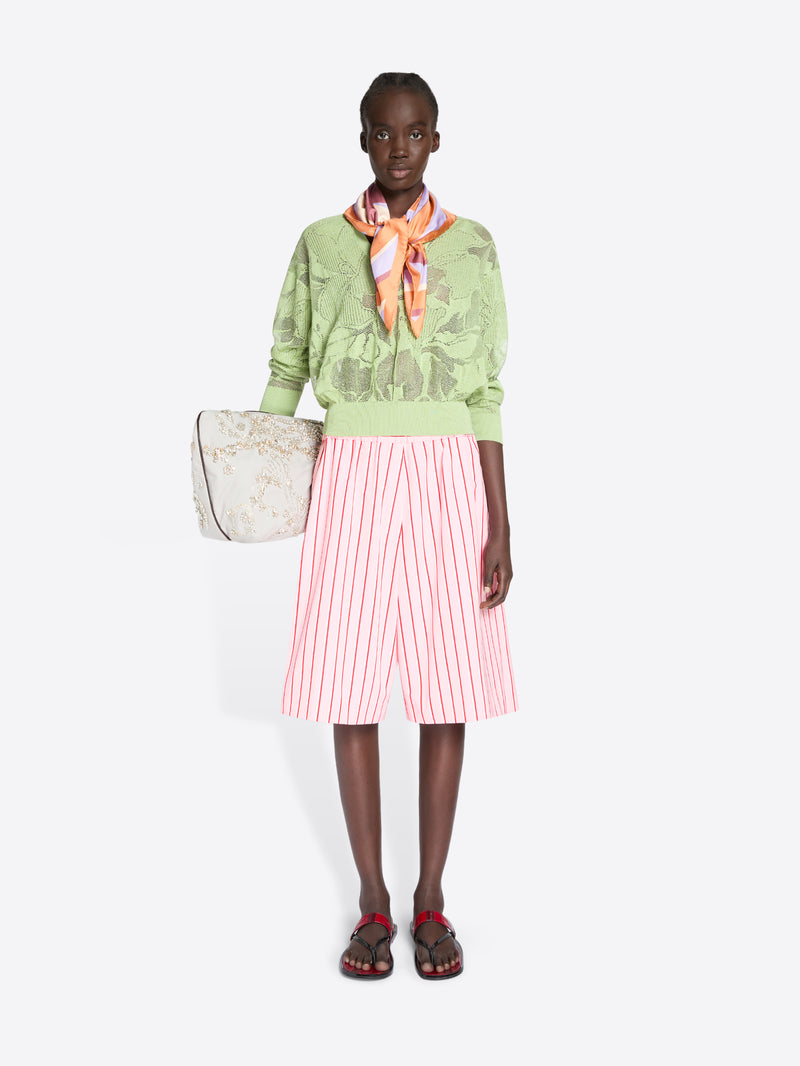 Model wearing a green sweater, pink striped skirt, and carrying a beige tote bag on a white background - Dries Van Noten