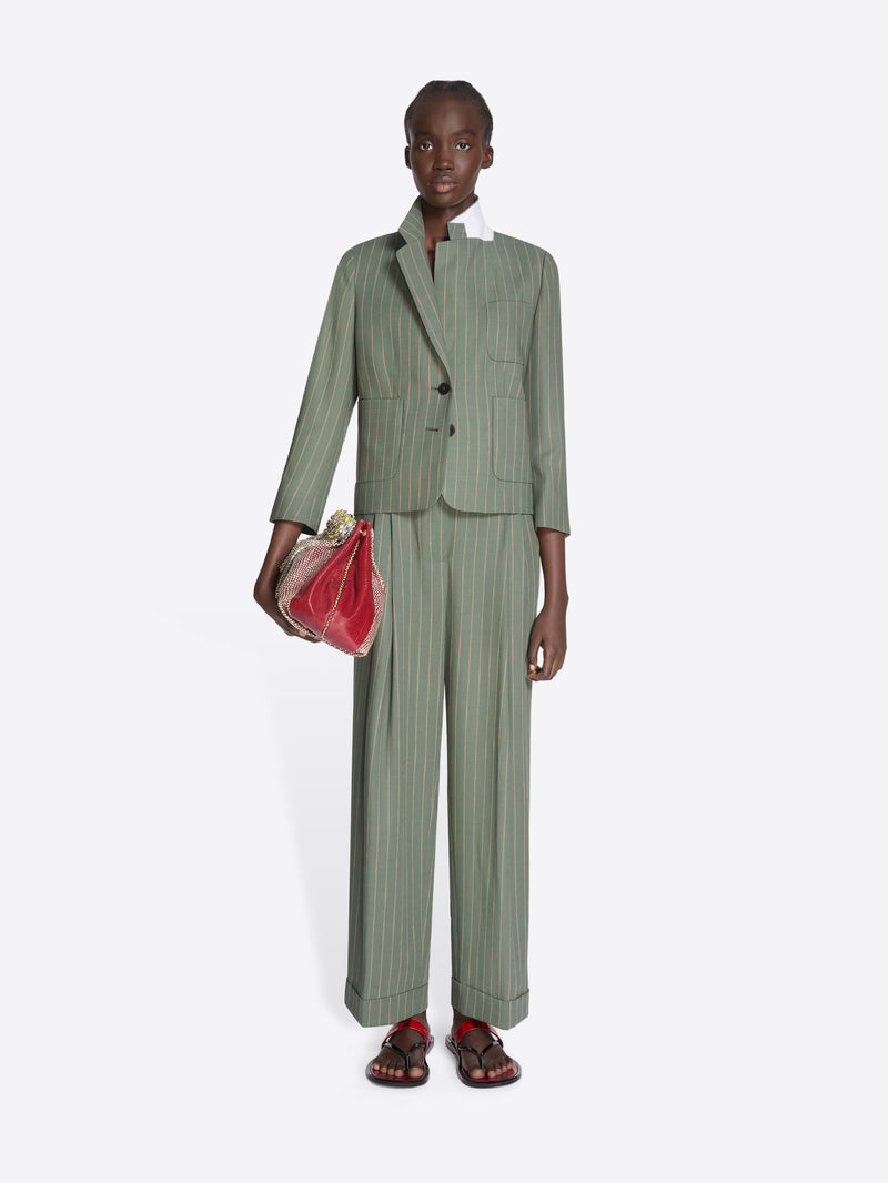 Person wearing a green pinstripe suit holding a red clutch on a white background - Dries Van Noten