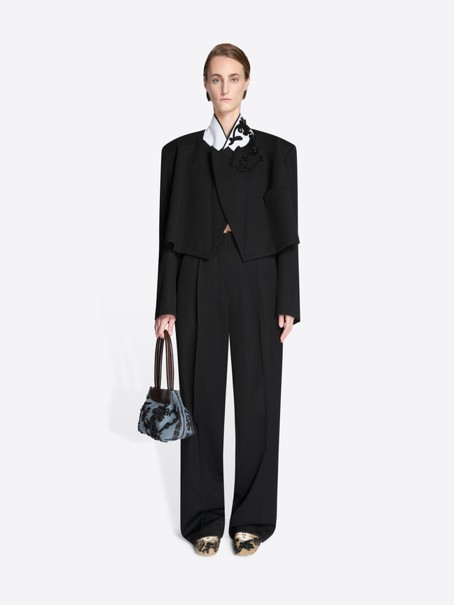 Person wearing a black outfit while holding a small bag on a light gray background - Dries Van Noten