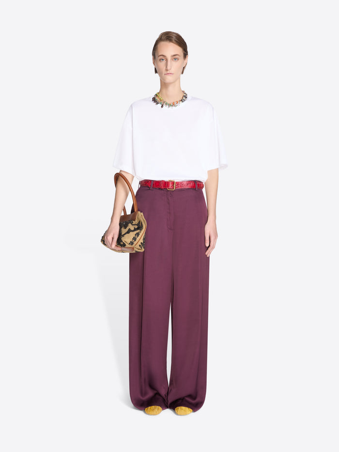 Model wearing a white top and burgundy pants with a small handbag on a light gray background - Dries Van Noten