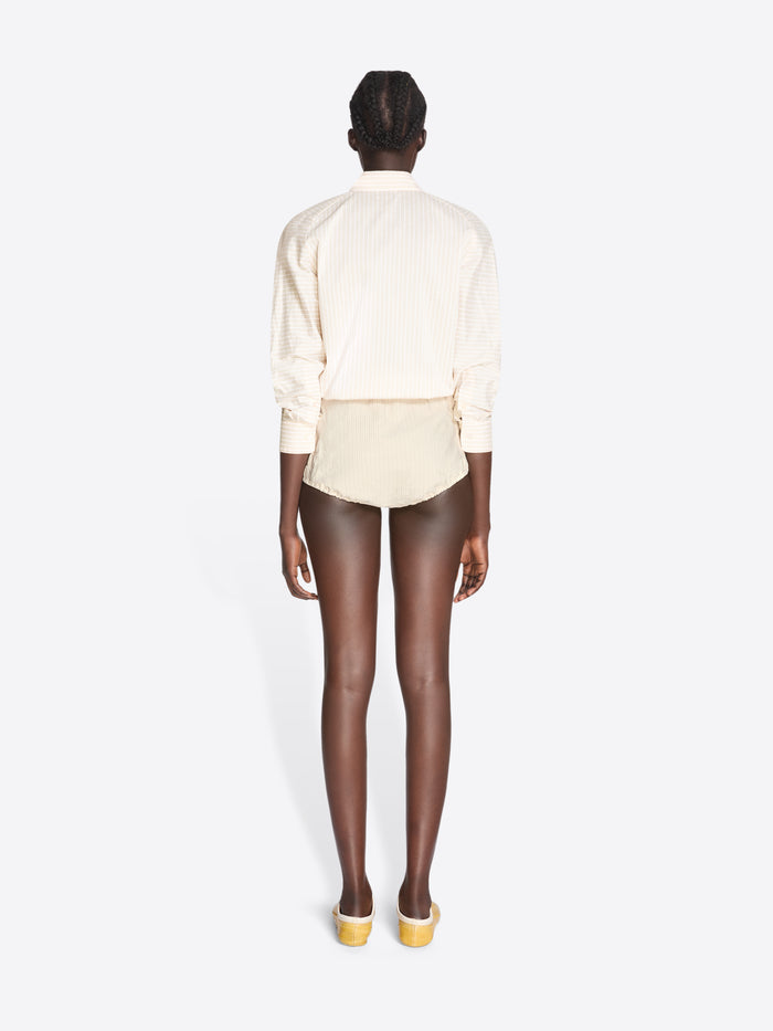 Person wearing a white blouse and beige shorts on a white background - Dries Van Noten