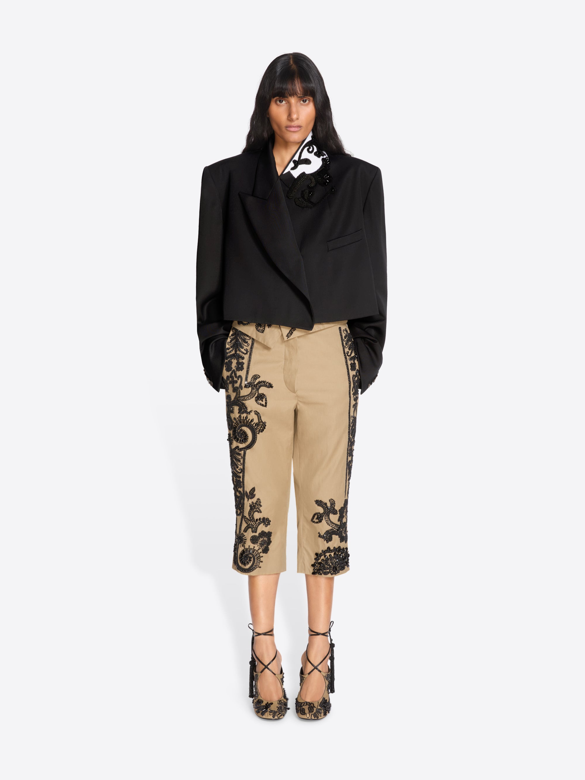 Woman wearing a black blazer and beige pants with black lace details on a white background - Dries Van Noten