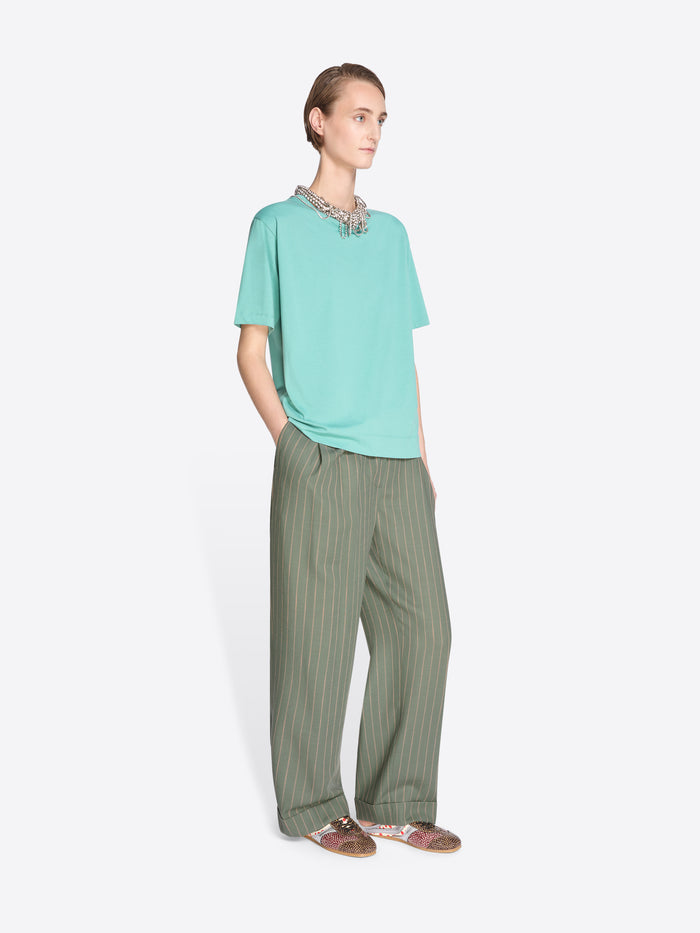 Person wearing a light blue shirt and green striped pants on a white background - Dries Van Noten