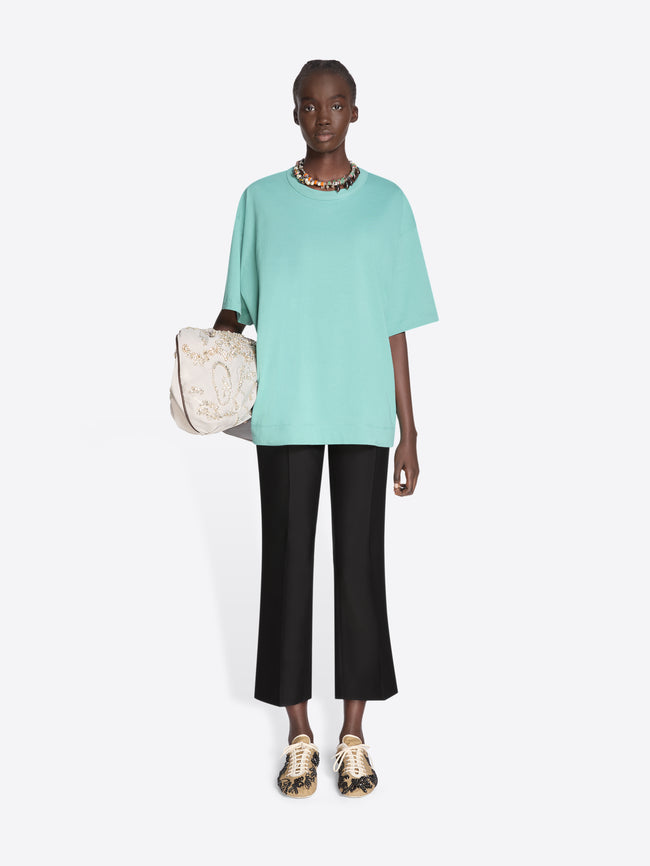 Person wearing a light blue top and black pants holding a beige bag on a white background - Dries Van Noten