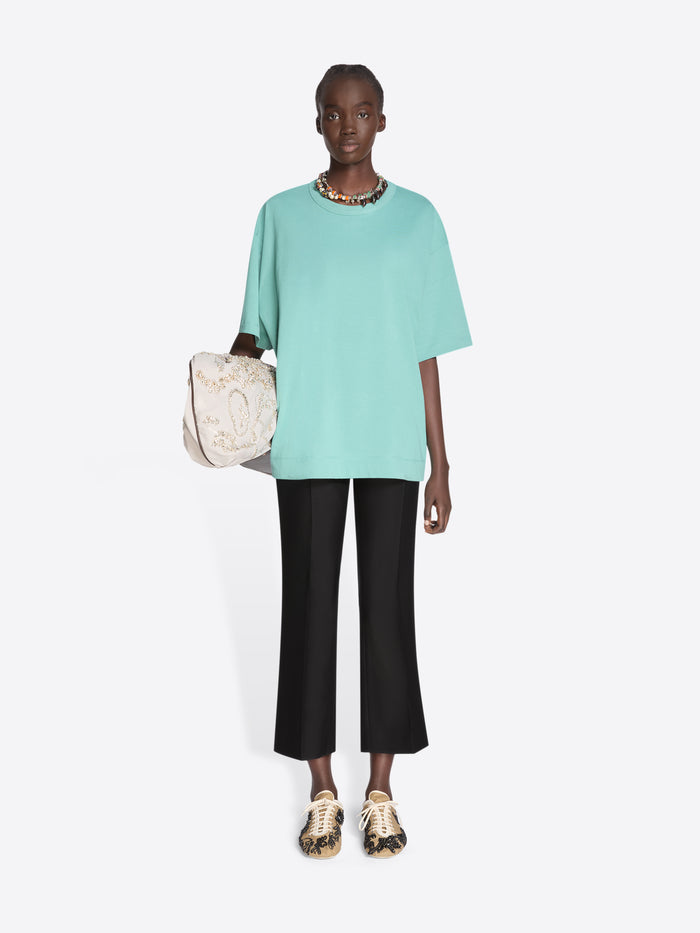 Person wearing a light blue top and black pants holding a beige bag on a white background - Dries Van Noten