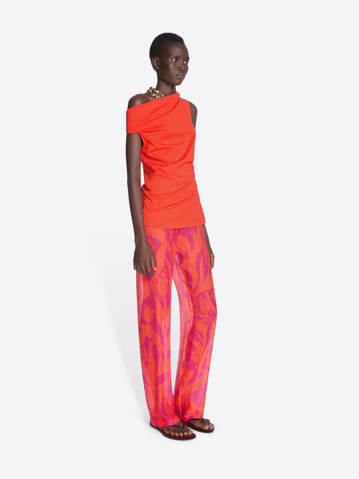 Model wearing a bright orange one-shoulder top and pink patterned pants on a white background - Dries Van Noten