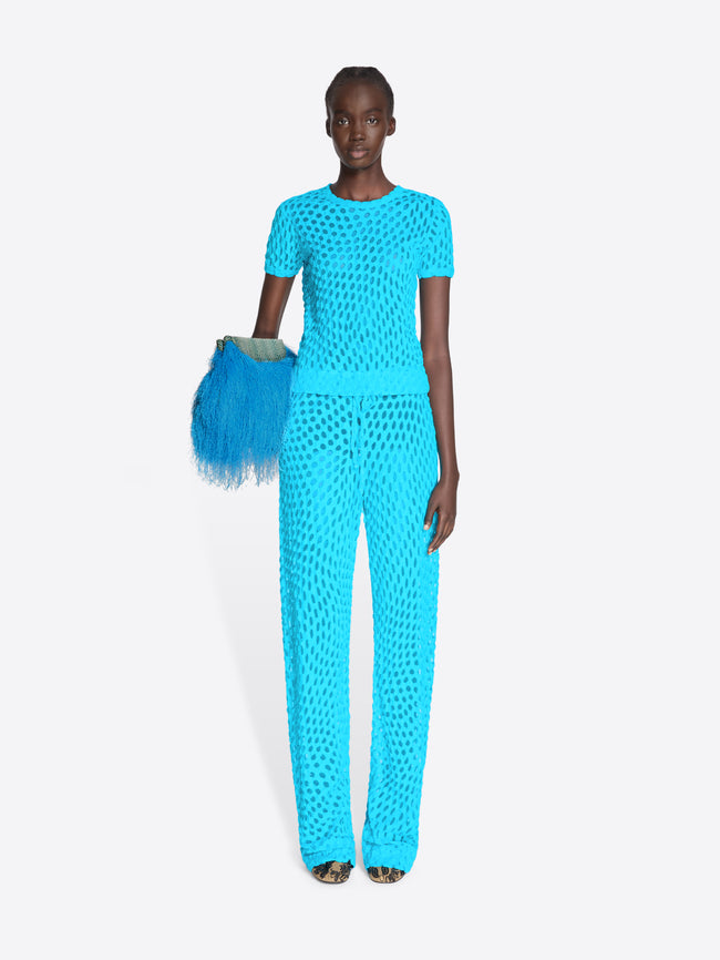 Model wearing a turquoise outfit with matching clutch against a white background - Dries Van Noten