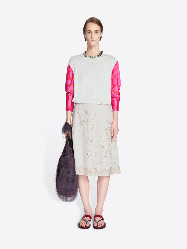 Model wearing a white top with pink sleeves and a beige skirt, holding a dark purple bag on a white background. - Dries Van Noten