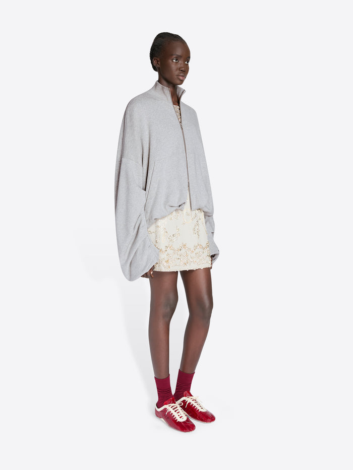 Person wearing a light gray oversized shirt, white lace skirt, and red sneakers on a white background - Dries Van Noten
