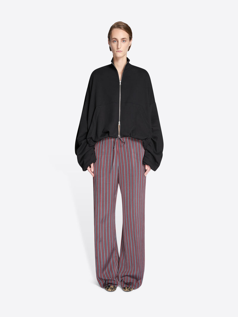 Person wearing a black jacket and striped pants on a white background - Dries Van Noten