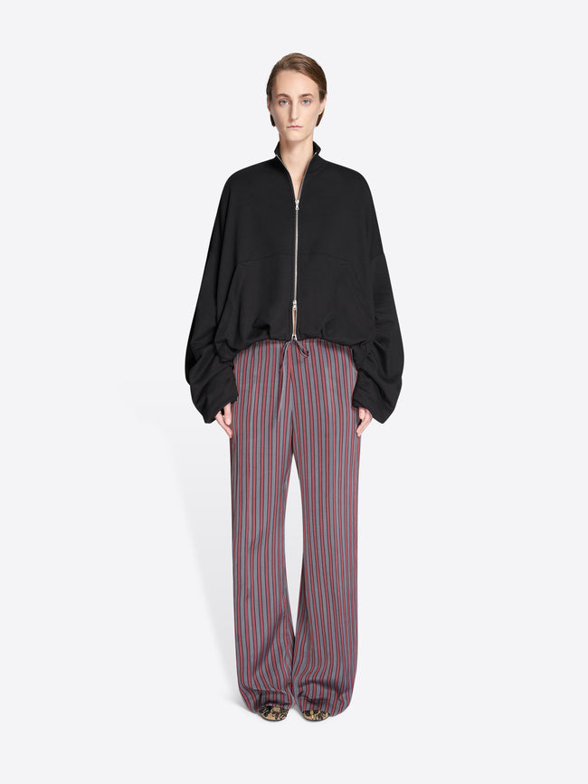 Person wearing a black jacket and striped pants on a white background - Dries Van Noten