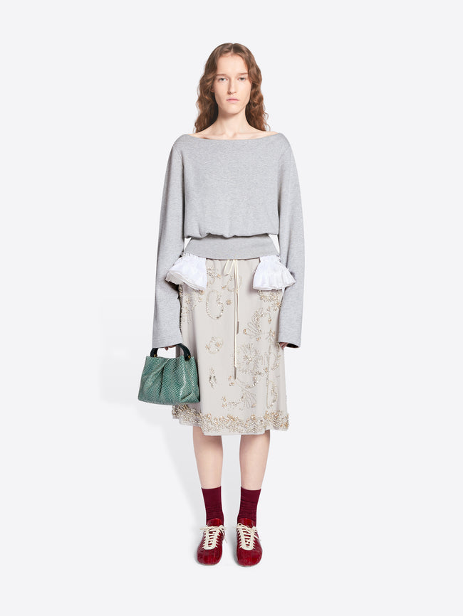 Woman wearing a light gray sweater, patterned skirt, and red shoes on a white background - Dries Van Noten