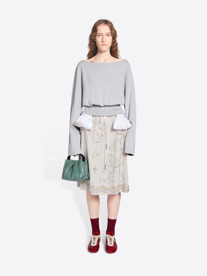 Woman wearing a light gray sweater, patterned skirt, and red shoes on a white background - Dries Van Noten