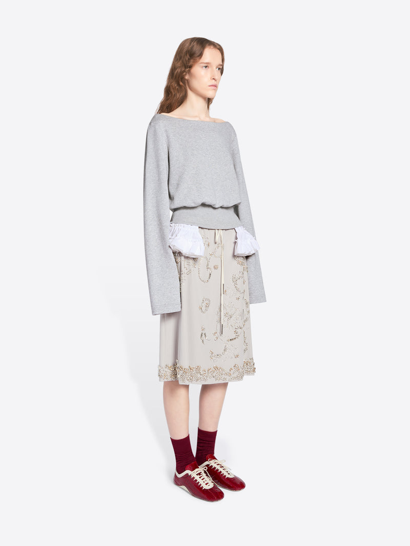 Woman wearing a light gray sweater, beige patterned skirt, and red shoes on a white background - Dries Van Noten