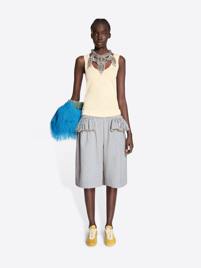 Model wearing a sleeveless top with embellishments and a layered skirt, holding a blue feathered bag on a white background. - Dries Van Noten